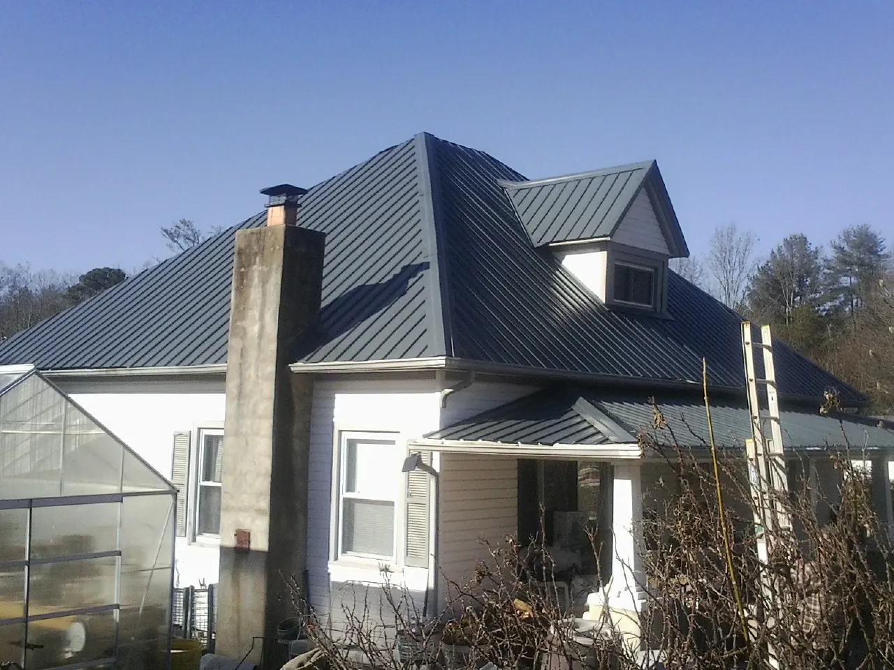 Dark blue standing seam metal roof on a white farmhouse with dormer — Slate & Tile Roof Repair by Roofing Brothers in Valley Falls