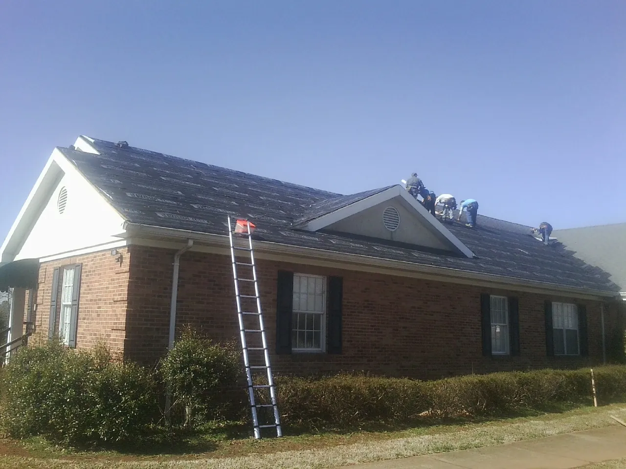 Crew tearing shingles off a brick ranch roof with a ladder set — Metal Roof Repair work by our crew in Valley Falls