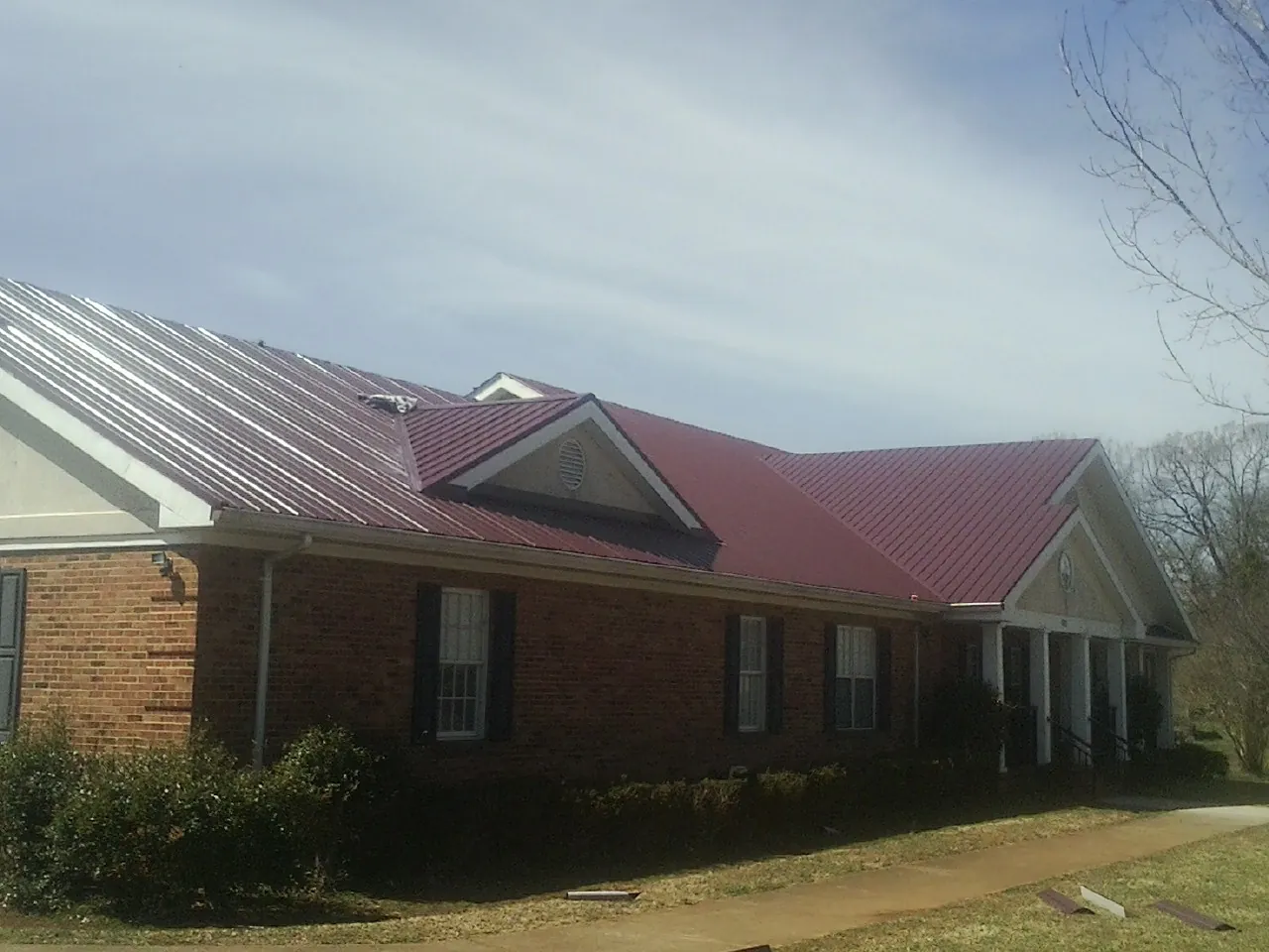 Red metal roof with gabled entries on a long brick building, from a Hail Damage Roof Repair job in Valley Falls
