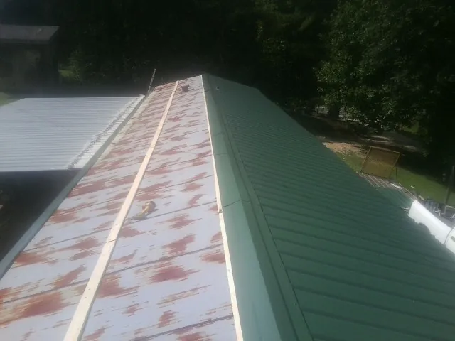 Old rusted panels beside newly installed green metal roofing — Wind Damage Roof Repair by Roofing Brothers in Valley Falls