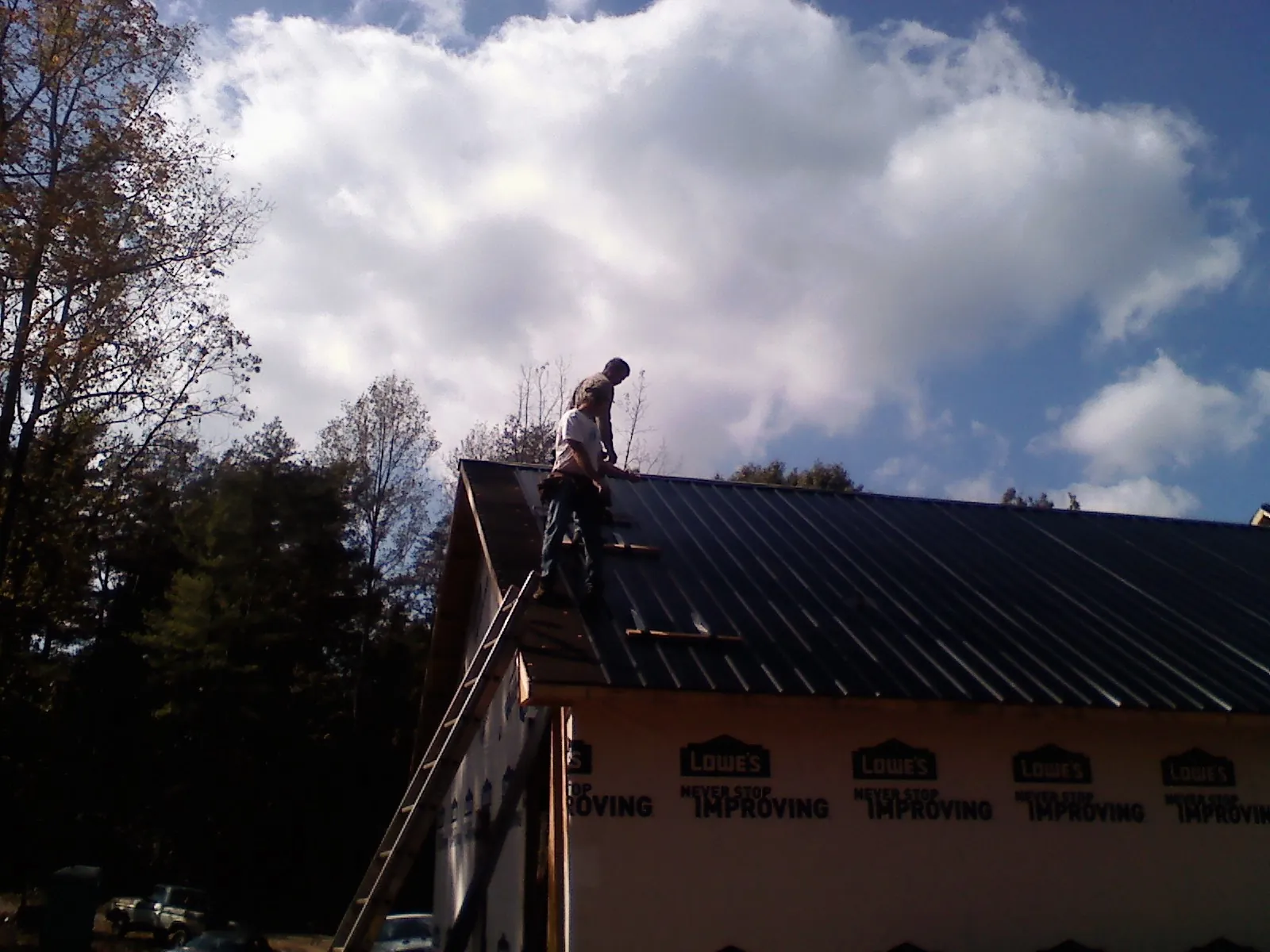 Roofer fastening dark metal panels high against a cloudy sky, from a Roof Inspection job in Valley Falls